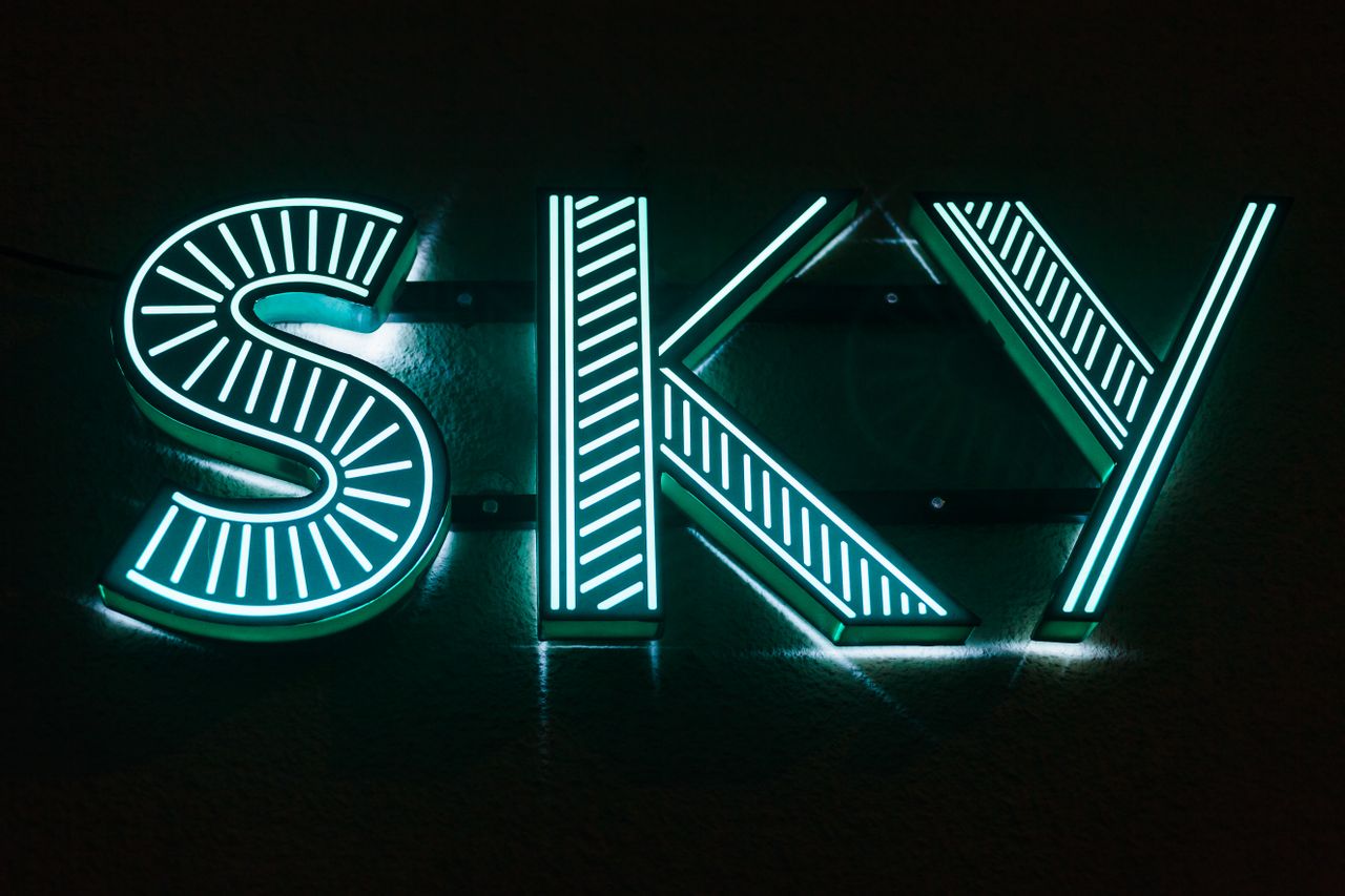 Illuminated neon sign displaying SKY in a dark setting, glowing blue-green.
