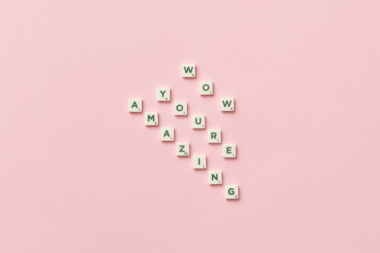 Motivational message formed with alphabet tiles on a pastel pink background.