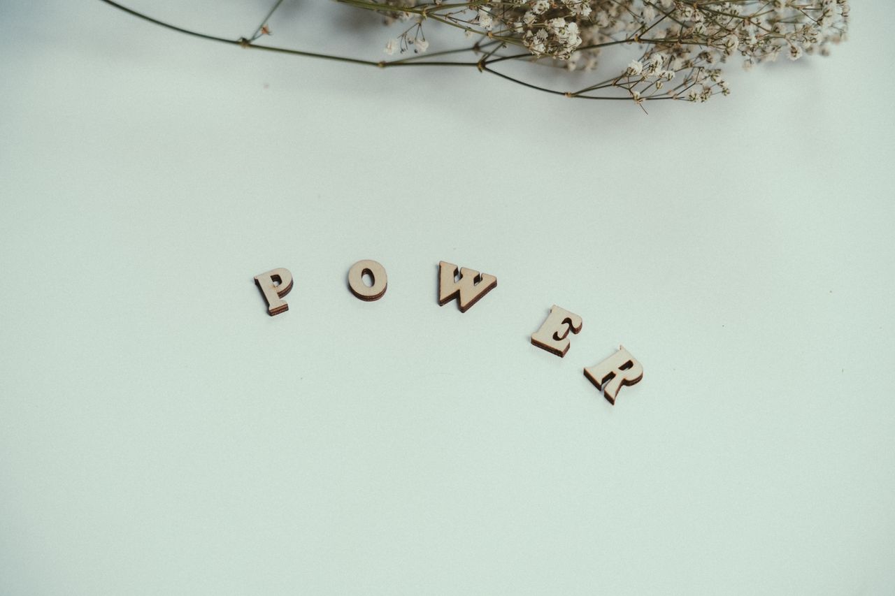 Minimalist photo of wooden letters spelling POWER with a floral accent.